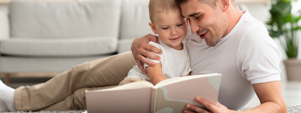 parenting books - the photograph shows a man and baby lying on the floor together looking at a book.
