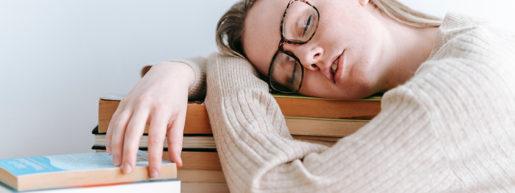 parenting books - the photograph shows a woman asleep with her head on a pile of books