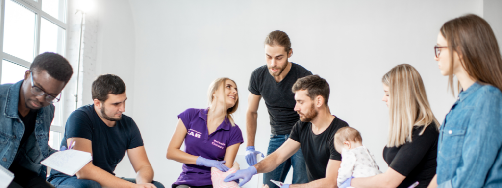 pregnancy classes - the image shows a group of people sitting round in a circle looking at a baby doll
