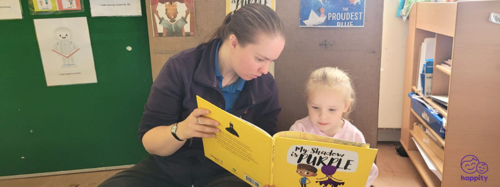 LGBTQ+ children's books - the photograph shows a nursery practitioner reading 'My Shadow is Purple' to a child.