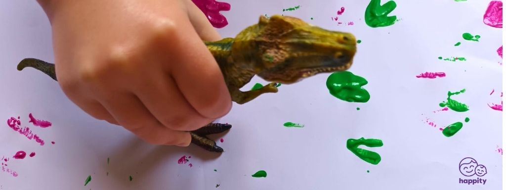 dinosaur activities for toddlers - the photograph shows a child making dinosaur footprints on a piece of paper using a toy dinosaur